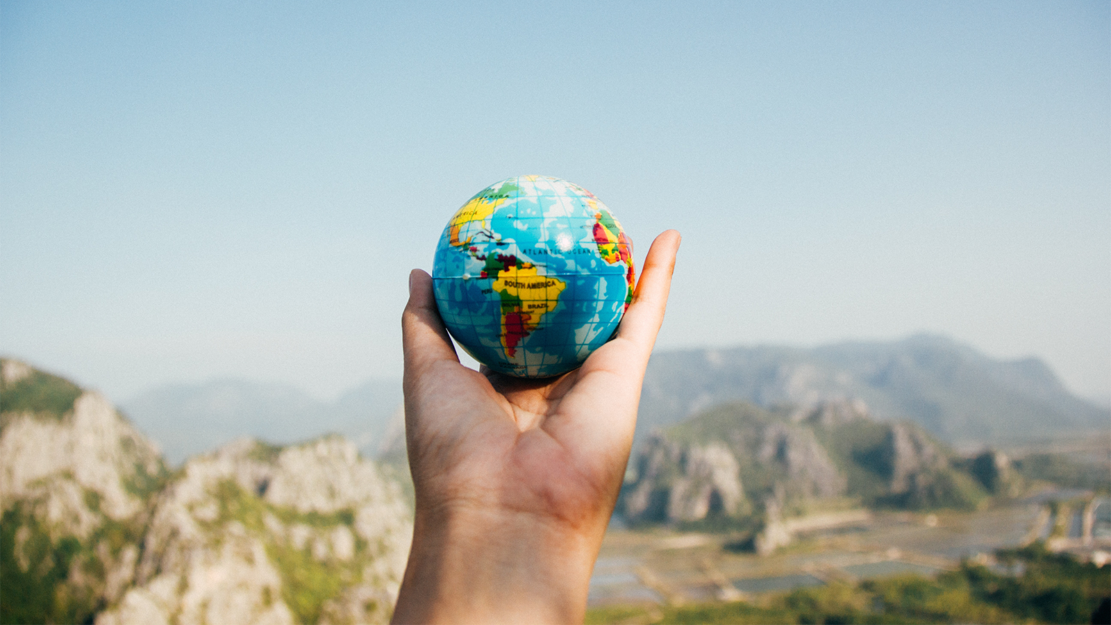 hand holding a mini globe up in front of a scenic landscape